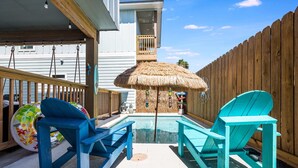 A pool area with two blue Adirondack chairs, a thatched umbrella, and a wooden deck.