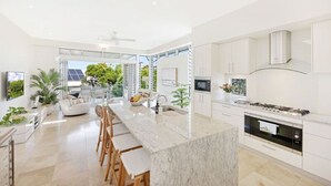 Een moderne keuken met een marmeren eiland, witte kasten en een groot raam met uitzicht op groen.