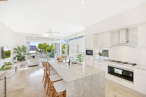 Una cocina moderna con una isla de mármol, armarios blancos y un amplio ventanal con vistas a la vegetación.