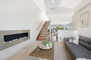 A modern living room with a fireplace, a sofa, a coffee table with plants, and a staircase leading to an upper level.