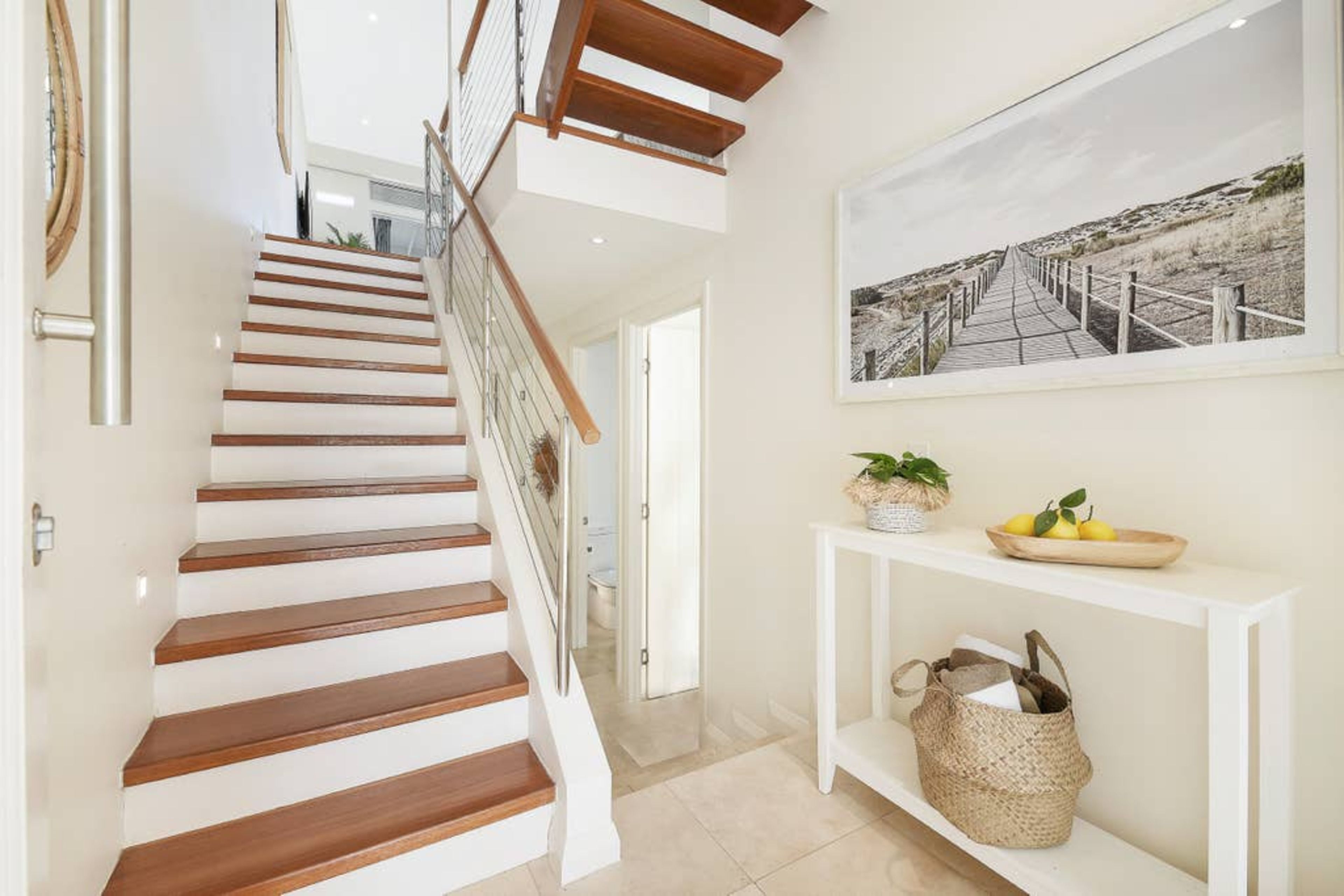Eine Treppe mit Holzboden und Glastrennwand führt zu einem Flur, in dem ein weißer Konsolentisch und ein gerahmtes Bild an der Wand stehen.