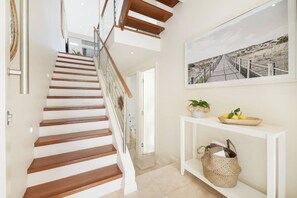 A staircase with wooden steps and a glass railing, leading to a hallway with a white console table and a framed picture on the wall.