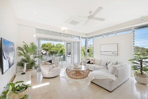 A spacious living room with a ceiling fan, large windows, and a view of greenery outside. - Soul on Sunshine - Divine Sunshine Beach villa (Sunshine Beach)