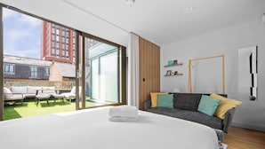 A modern bedroom with a large bed, a sofa, and a sliding glass door leading to a balcony. - 4 Bed Canal St Villa | Free Parking (Manchester)