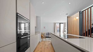 A modern kitchen with white cabinetry, a built-in oven, and a wooden floor. - 4 Bed Canal St Villa | Free Parking (Manchester)