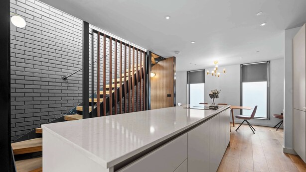 A modern kitchen with a central island, wooden staircase, and a dining area with a view. - 4 Bed Canal St Villa | Free Parking (Manchester)