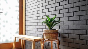 A wicker plant stand with a potted plant against a brick wall, a wooden bench, and a window with blinds. - 4 Bed Canal St Villa | Free Parking (Manchester)