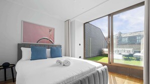 A bedroom with a large bed, a view of a patio with outdoor furniture, and a brick wall. - 4 Bed Canal St Villa | Free Parking (Manchester)
