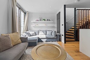 Un salon moderne avec un canapé gris, une table basse ronde et un escalier menant à une mezzanine.