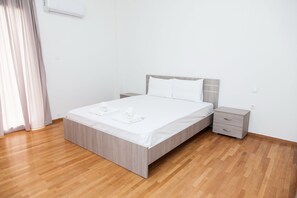 Un dormitori modern amb terres de fusta, un llit amb roba blanca, una tauleta de nit i aire condicionat fixat a la paret.