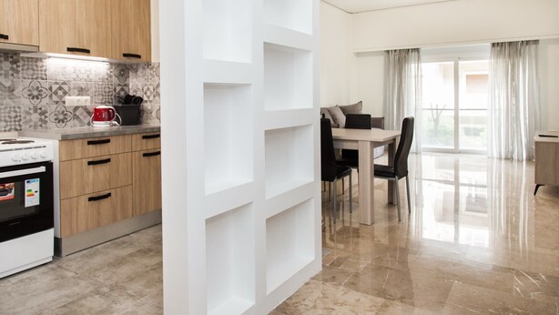 A modern kitchen with wooden cabinets, a white backsplash, and a dining area with a table and chairs. - Glamorous Apt in central Athens (Athens)