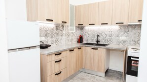 A modern kitchen with light wood cabinets, a white refrigerator, a black coffee maker, and a built-in oven. - Glamorous Apt in central Athens (Athens)