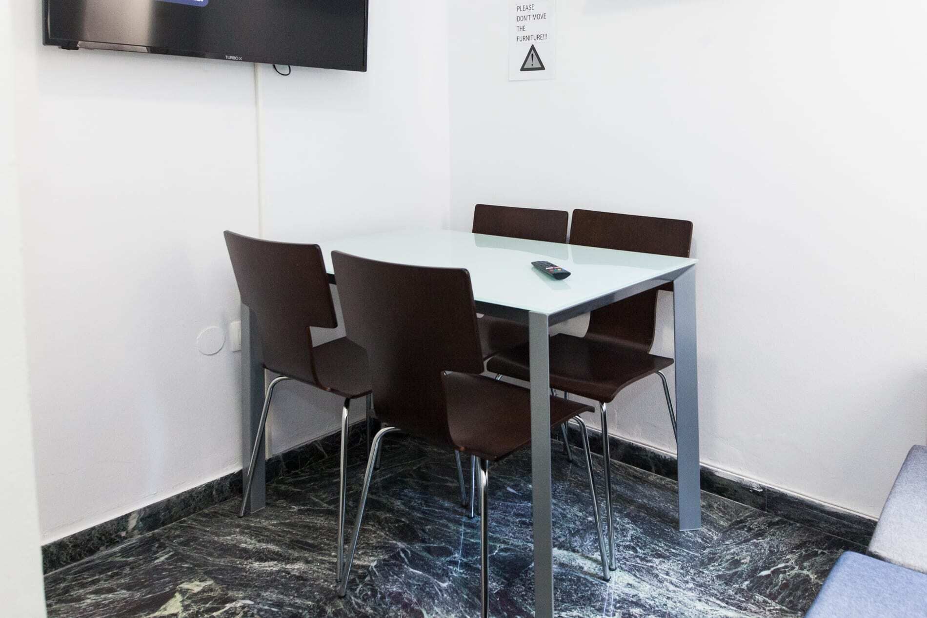 A conference room with a white table, six brown chairs, a TV mounted on the wall, and a warning sign.
