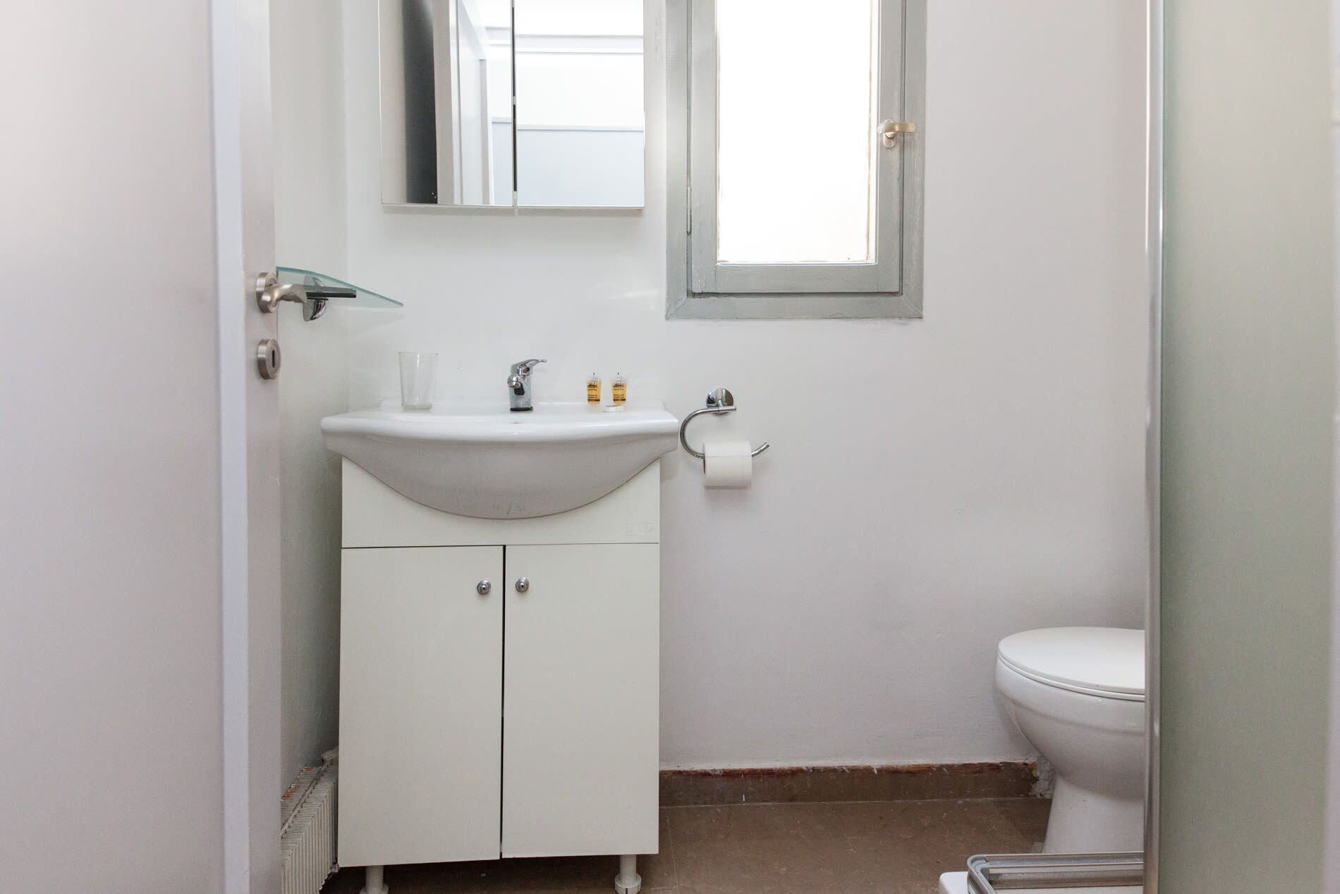 Ein kleines, weißes Badezimmer mit Waschbecken, Toilette und einem Spiegel über dem Waschbecken.