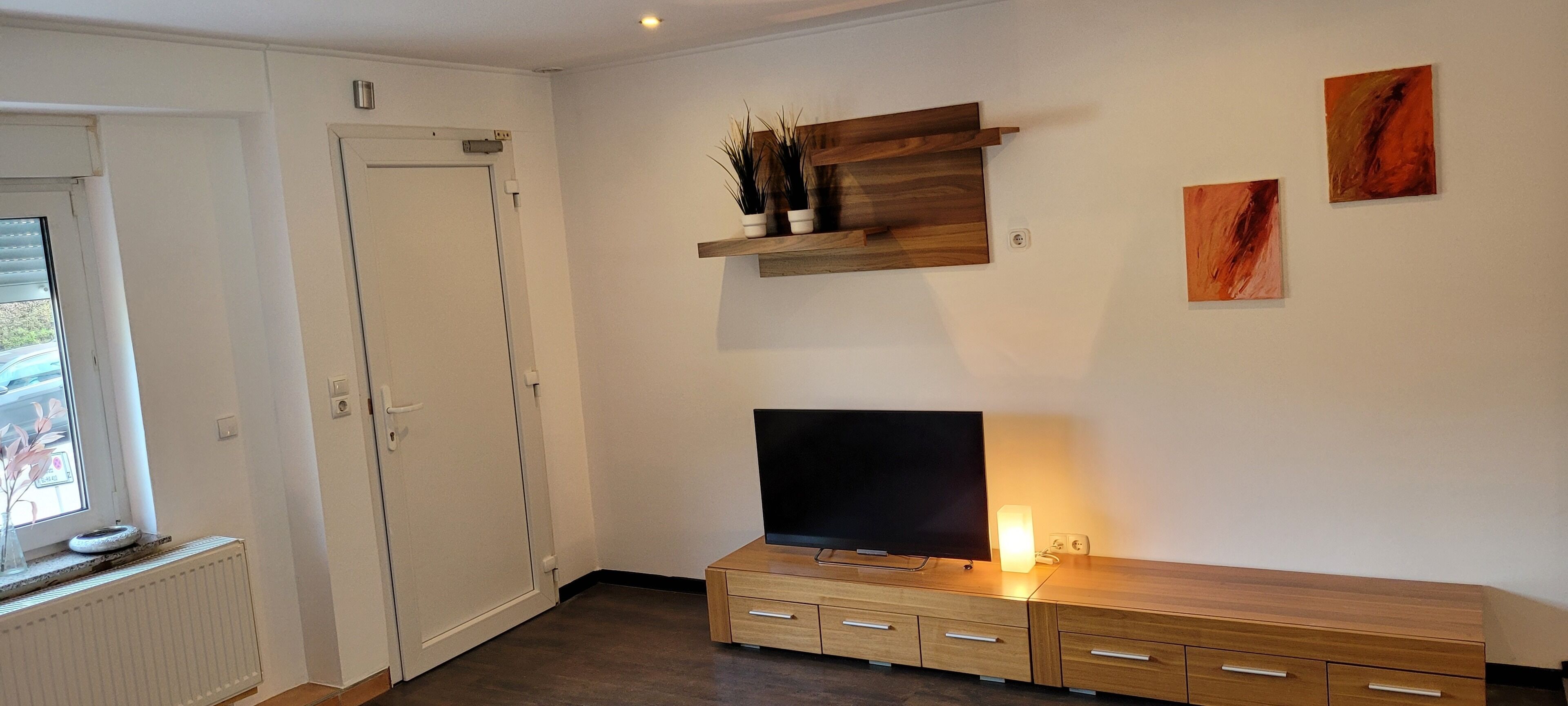 Un salon moderne avec un téléviseur, un meuble de rangement en bois et des œuvres d’art accrochées au mur.