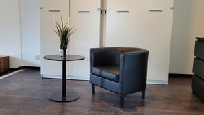 A modern room with a dark wood floor, a black leather chair, a small round table with a potted plant, and a white wardrobe with a door.