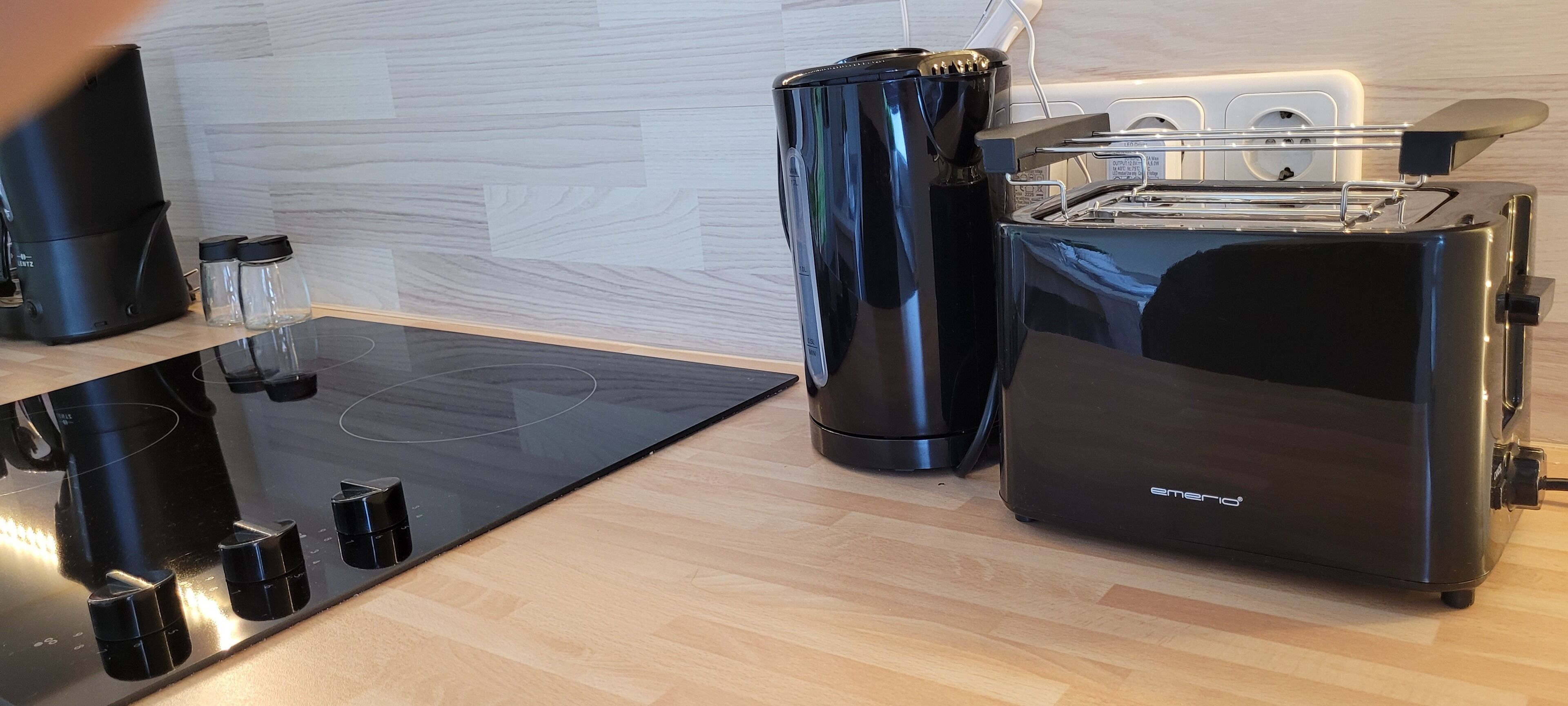 Een moderne keuken met een zwarte inductiekookplaat, een zwarte koffiezetapparaat, een zwarte prullenbak en een zwarte broodrooster.