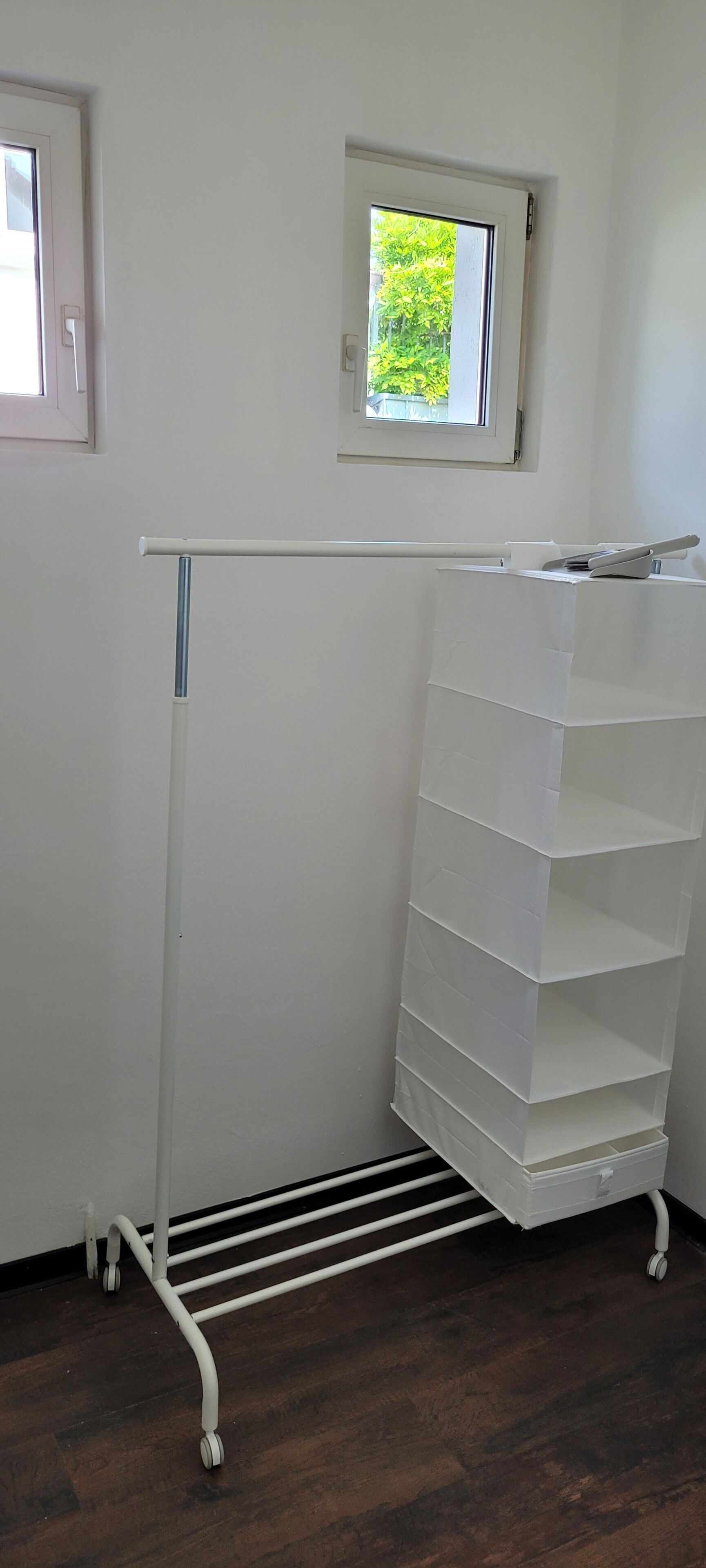 Ein weißer Stauraum mit mehreren Regalen und einer ausziehbaren Ablage, platziert vor einer Wand mit einem kleinen Fenster.