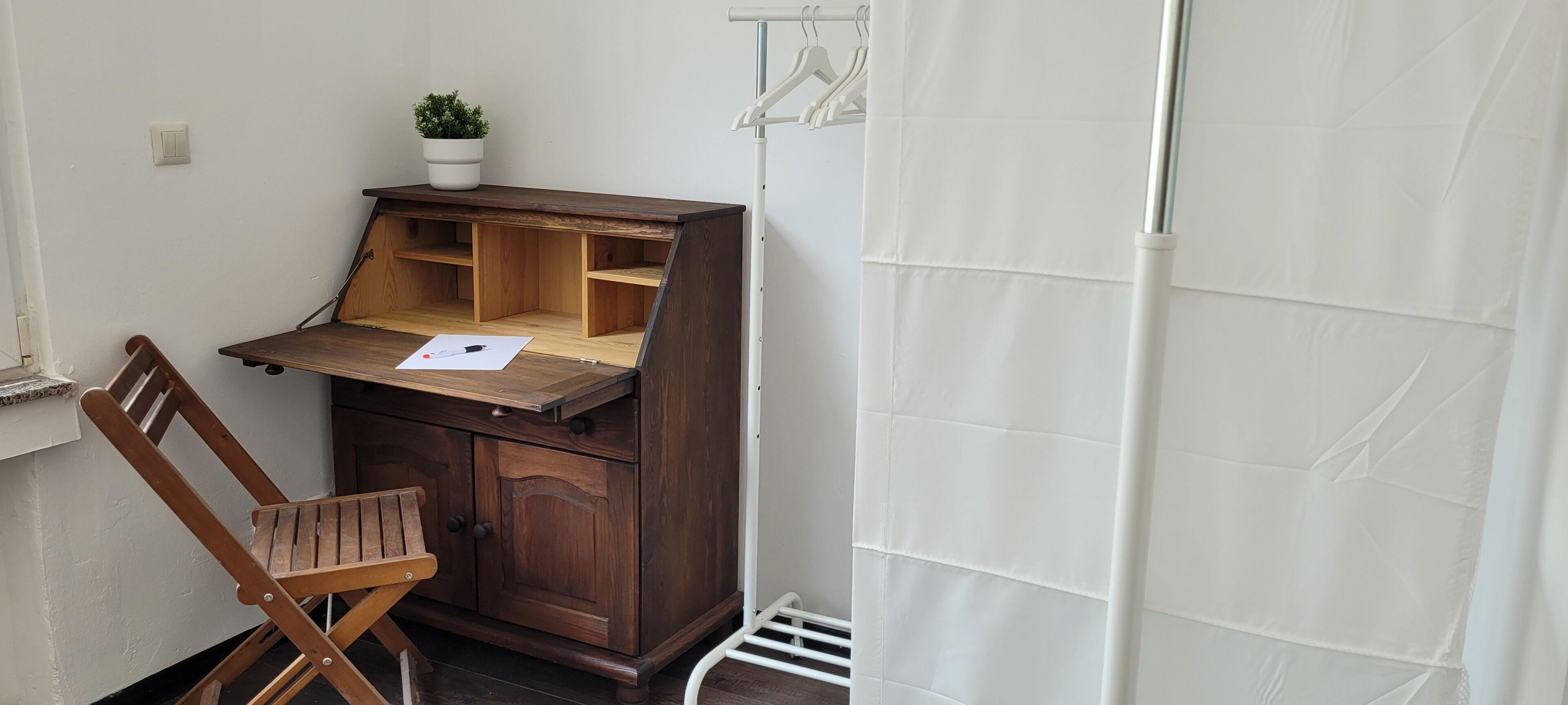Un'area di lavoro compatta con una scrivania in legno, una sedia e una pianta in vaso.