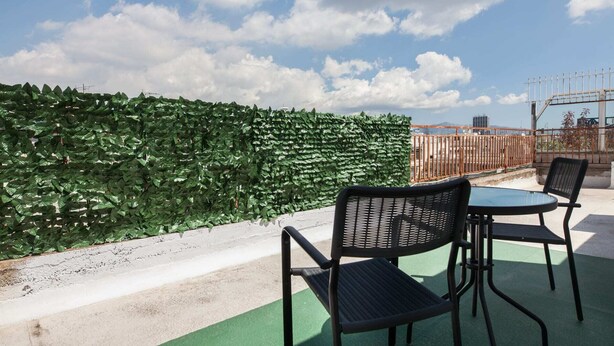 A rooftop terrace with a green hedge, two black wicker chairs, and a small round table. - Retire with Outstanding Lycabettus View (Athens)
