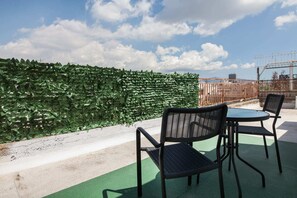 Terraço no telhado com um muro verde, duas cadeiras de vime preto e uma pequena mesa redonda.