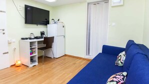 A compact room with a kitchenette, a blue sofa, and a television. - Retire with Outstanding Lycabettus View (Athens)