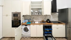Una cuina compacta amb armaris blancs, forn integrat, microones, rentaplats i un rentamans.