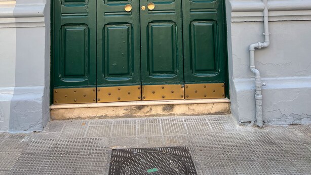 Una porta doble de color verd amb pomes de llautó, un petit cartell taronja a la part superior i una placa amb el número '163' a la paret.