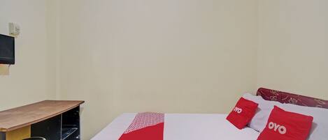 A hotel room with a bed, two red pillows with the word "OYO" on them, a wooden desk, and a small stool.
