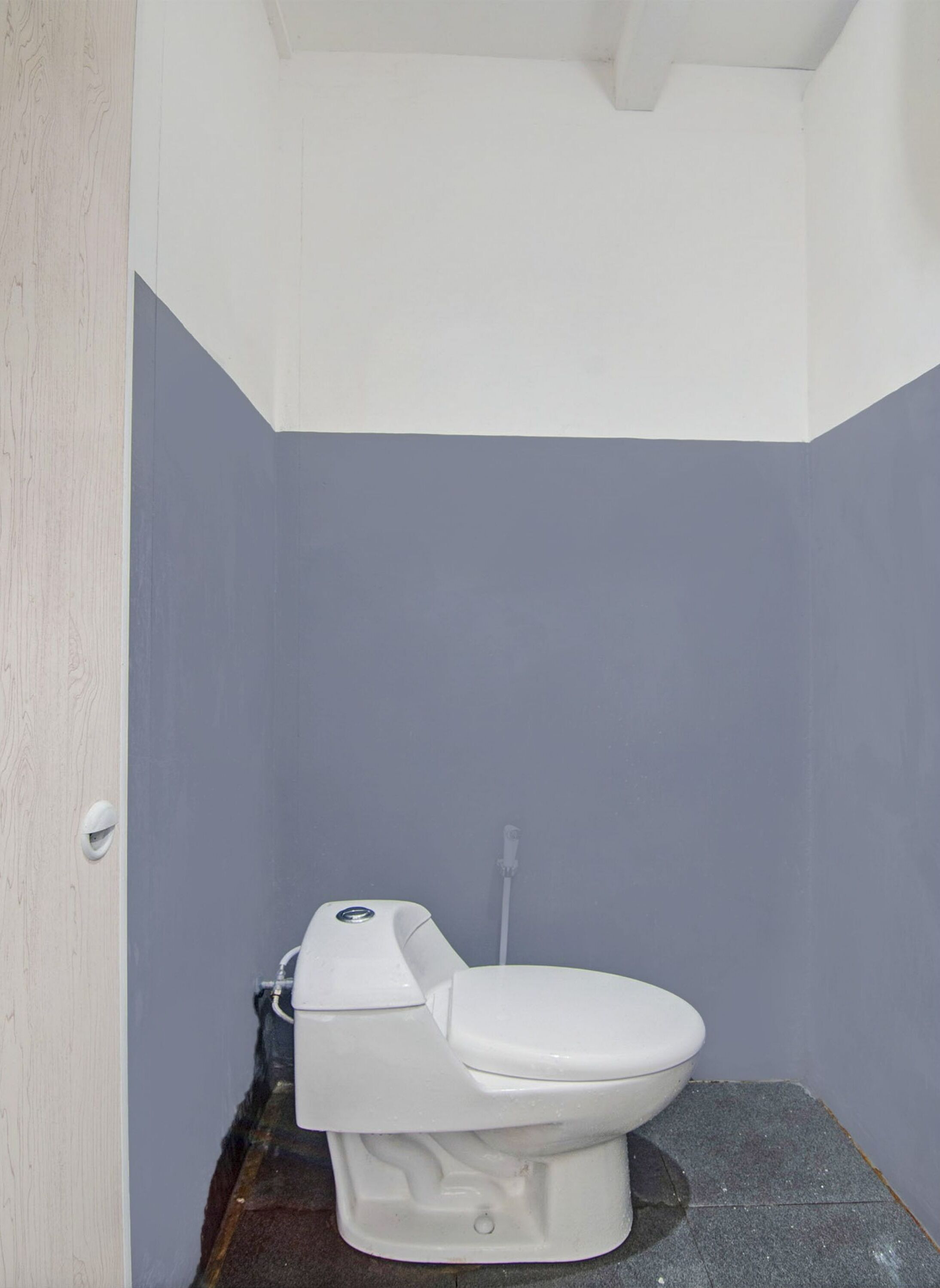 Une petite salle de bain étroite, avec des toilettes blanches et un sol gris.