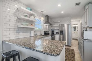 Uma cozinha moderna com azulejos brancos tipo metrô, bancadas de granito, eletrodomésticos de aço inoxidável e prateleiras embutidas.