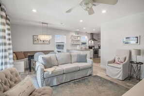 Uma sala de estar moderna com sofá, poltronas, um lustre e um ventilador de teto.