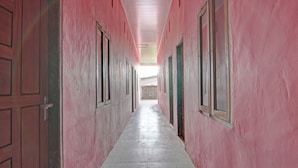 Un long couloir étroit aux murs roses et aux portes en bois, qui mène à un espace lumineux au bout.