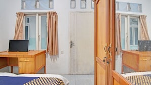 Une pièce comprenant deux bureaux en bois, chacun équipé d’un ordinateur portable, une grande armoire et un lit recouvert d’une couvre-lit à pois.