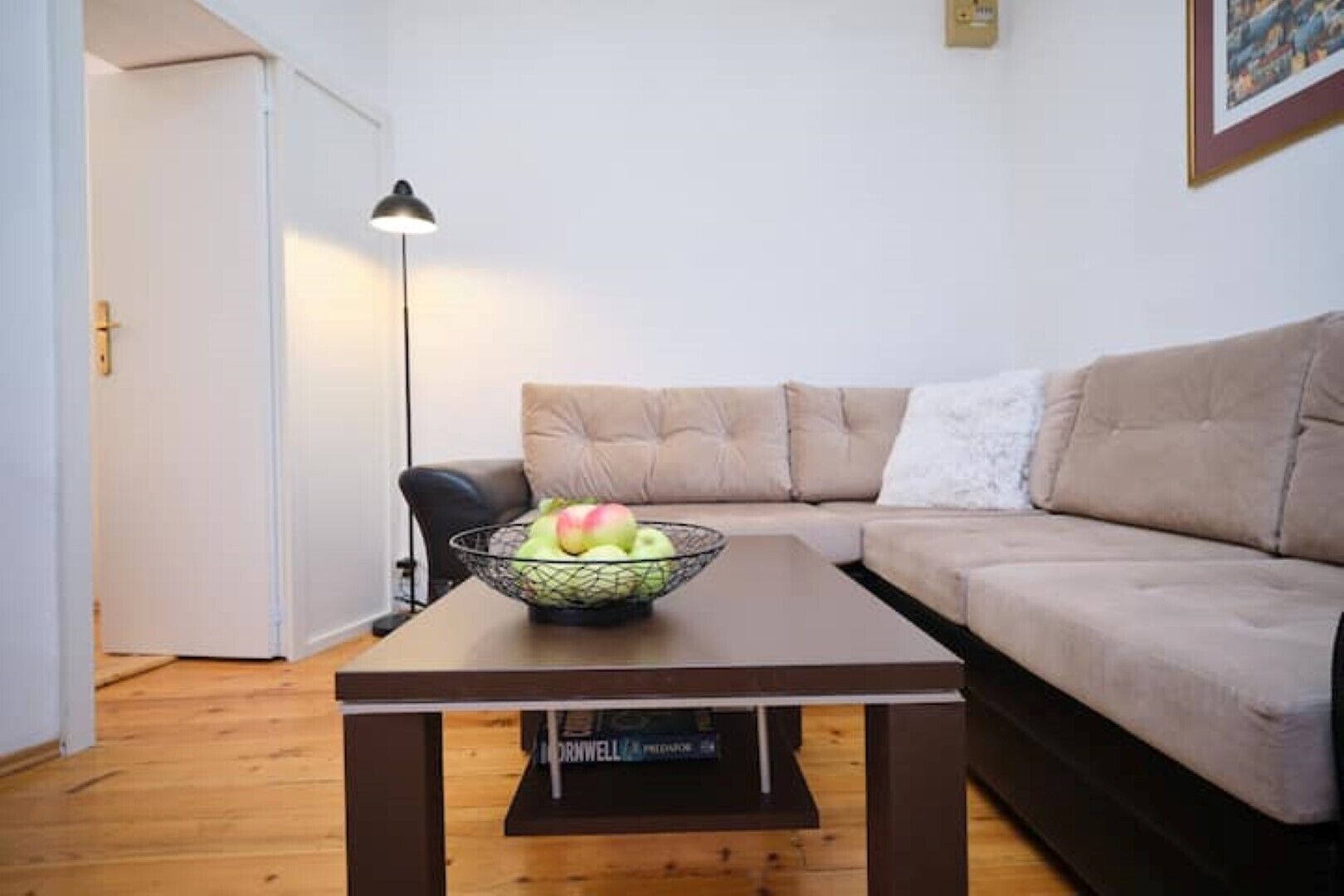 A living room with a beige sofa, a coffee table with a fruit bowl, and a floor lamp.