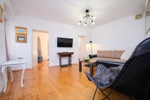 Una sala de estar con suelo de madera, un sofá, un televisor, una mesita y una silla.