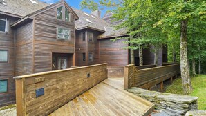 A wooden cabin with a deck and stone steps leading to a covered area. - Captivating Condo with sports & fitness center, pool, and hot tub - Highridge E10 (Killington)