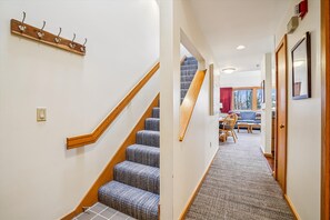 A staircase with wooden handrails and carpeted steps leading to a room with a sofa, table, and window.
