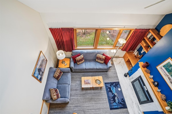 Een moderne woonkamer met een hoekbank, een salontafel en een uitzicht op de natuur door grote ramen.