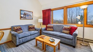 A living room with two grey sofas, a wooden coffee table, a lamp, and a painting on the wall. - Captivating Condo with sports & fitness center, pool, and hot tub - Highridge E10 (Killington)