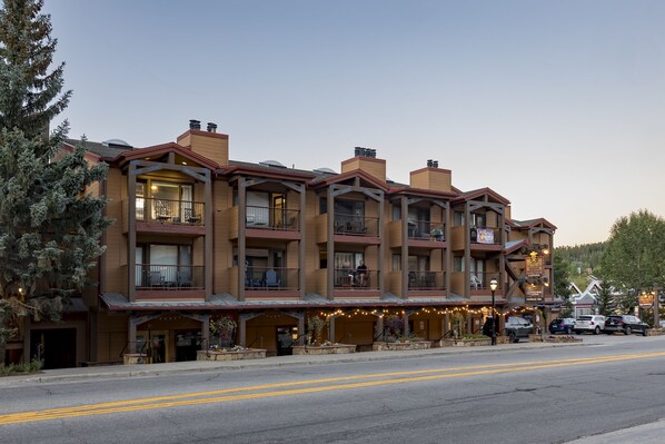 A multi-story hotel with balconies, a ground-level restaurant with outdoor seating, and a street view with parked cars.