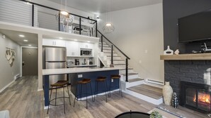 Una cocina moderna con una isla central, taburetes de bar, una escalera y una chimenea.