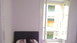 A bedroom with a bed, two pillows, a radiator, and a window with a view of a balcony. - Charming flat center and near the lake  (Genève)