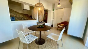 A dining area with a round table, white chairs, a woven hanging light fixture, and a rustic stone wall.