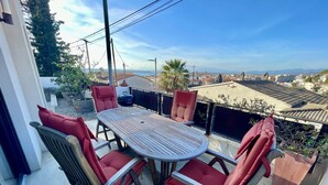 A balcony with a round table and four chairs, overlooking a cityscape with buildings and a clear sky.