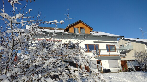 A two-story house with a balcony, a garage, and a snow-covered yard.