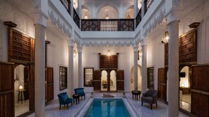 Un área de piscina interior lujosa con columnas ornamentales, puertas de madera y elegantes luminarias.