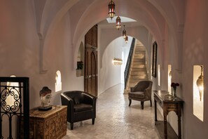 An arched hallway with a staircase, leather armchairs, a wooden cabinet, and wall-mounted sconces. - Riad Spice by Marrakech Riad (Marrakech)