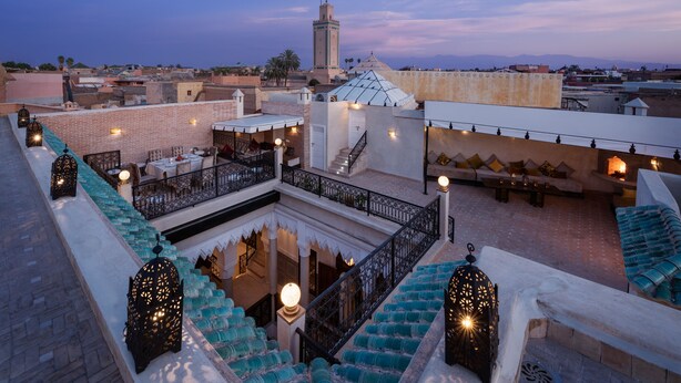 Una terraza en la azotea con un patio central, zonas de estar y vistas a una mezquita y al paisaje urbano.