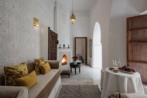 A cozy living room with a sofa, a fireplace, a dining table with fruit, and a patterned wall.